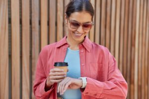 Mulher de óculos escuros olhando sorrindo para seu smartwatch